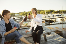 Smiling Male And Female Friends Toasting Beer Bottles At Harbor