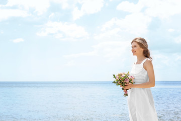 Wall Mural - Young bride in white gown holding bouquet on seashore