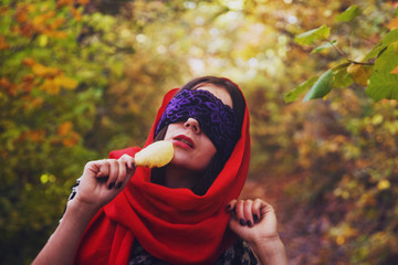 A girl with a blindfold holds a yellow autumn leaf in the forest at dawn