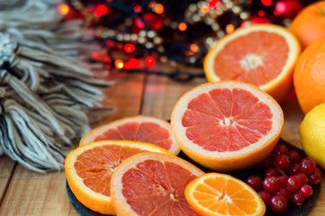 Citrus fruits on wooden table with woolen blanket and red christmas lights. Grapefruit, orange, tangerine and red currant. Christmas and new year celebration