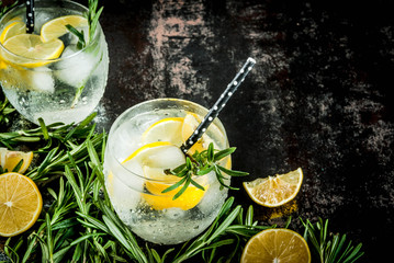 Cold lemonade or alcohol vodka cocktail with lemon and rosemary, On a black rusty metallic background, copy space top view