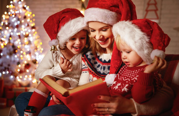 Wall Mural - family mother and children read a book at christmas near fireplace at home