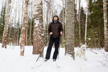 Young man cross-country skiing in the forest with White Swiss shepherd dog