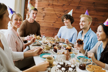 Wall Mural - Young companions gathered by birthday dinner having fun by festive table