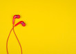 Bright red earbud headphones isolated on a bright yellow background with copy space on the right for your text (minimal concept, top view)