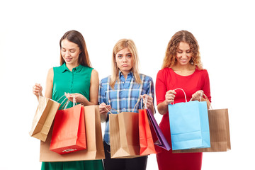 Wall Mural - Portrait of three young girlfriends holding bunches of multi-colored shopping bags