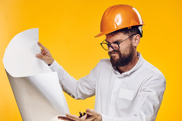 Engineer with a beard on a yellow background holds a drawing