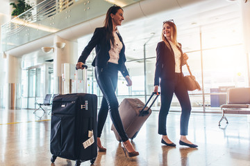 two stylish female travelers walking with their luggage in airport