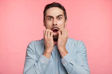 Wall Mural - Portrait of nervous bearded male student being in stupor, worries to hear results of test, stares at camera, wears formal shirt, isolated over pink background. Amazed surprised astonsihed man