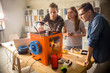 © Seventyfour - Three young engineers standing at wooden desk and using 3D printer in order make small prototypes, interior of modern laboratory on background