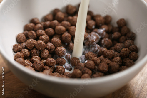 Fotografía pour milk onto chocolate cereal balls in white bowl for breakfast