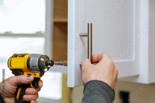 Fotografie, Obraz The worker sets a new handle on the white cabinet with a screwdriver