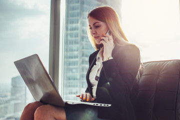 Young woman waiting in a hall sitting in modern office working on laptop talking on the phone