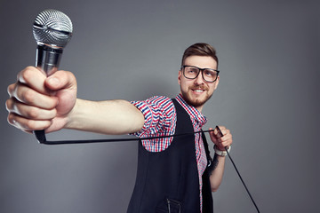 Karaoke man sings the song to microphone, singer with beard on grey background. Funny man in glasses holding a microphone in his hand at the karaoke singer sings the song