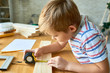 © Seventyfour - Side view portrait of cute little boy working with wood sitting at table and taking measurements  making wooden model