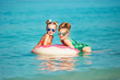 Two happy little girls rest on the sea. Smiling girl swimming in a circle in the sea
