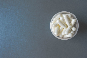 Close up of white pills or capsules in container or bottle on colorful background, medication or drug therapy concept, vintage view