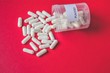 White placebo pills or capsules spilling out of bottle or white plastic container on colorful background, placebo treatment or effect concept