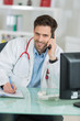 © auremar - young male doctor sitting at desk and phoning