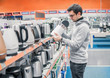 © Igor Kardasov - Smart young customer chooses a kettle in supermarket mall, at home electronics department, difficult decision. Various choice