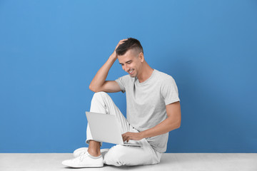 Young man with laptop sitting on floor near color wall
