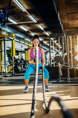 Wall Mural - Attractive strong fitness woman doing battle rope exercise in the modern sunny gym.