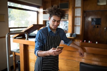 Smiling waiter using mobile phone at counter