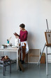 Female artist in her spacious white studio working with watercolor painting.  Natural lighting. Disclosure of creativity concept. Vertical composition with copy space