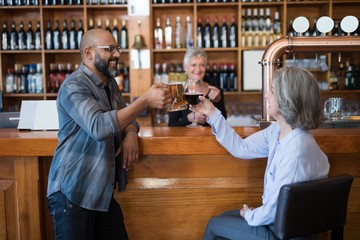 Wall Mural - Friends toasting glass of drinks at counter in bar