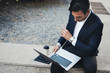 © SFIO CRACHO - Attractive elegant businessman using contemporary notebook and smartphone sitting outside.Blurred background. Horizontal.