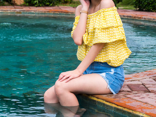 Young woman wearing hat enjoying and sitting on swimming pool edges in summer holidays or vacation .