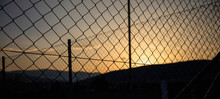 Steel Wire Mesh Fence On A Sunset Background. Blurred City And Hills Silhouette.