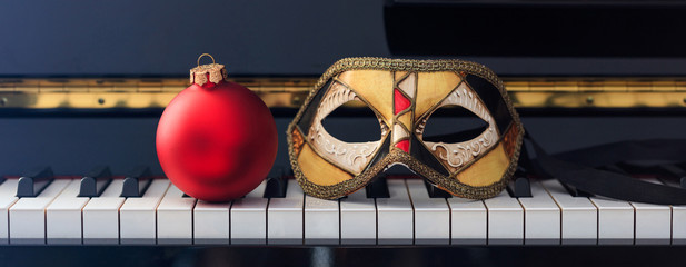 Red Chritmas ball and carnival mask on piano keyboard, front view