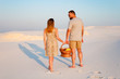 © ig_royal - lovely attractive couple on the white sand beach or in the desert or in the sand dunes, guy and a girl with a basket in their hands, the couple left traces or footprints on the sand, rear view