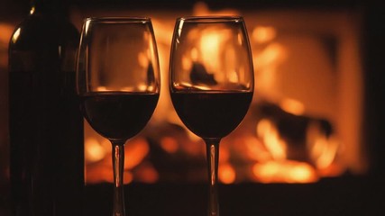 Wall Mural - Cinemagraph - Bottle and two red wine  wineglasses over fireplace background. Motion Photo.