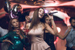 © VadimGuzhva - Young people have fun in a nightclub and sing in karaoke. In the foreground is a woman in a beige dress.