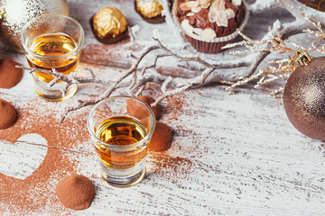 Whiskey or liqueur, truffle chocolate candies in cocoa powder and christmas decorations on white wooden background.