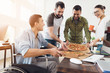 © VadimGuzhva - Office workers and man in a wheelchair are eating pizza. They work in a bright and modern office.