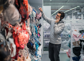 Happy smiling customer man choosing lingerie underwear for his wife in supermarket mall. speaks by mobile phone with wife or girlfriend.