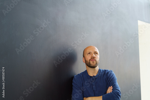 Fotomural mann lehnt mit verschränkten armen an einer wand und schaut kritisch nach oben