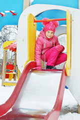 Cute little girl wearing bright pink clothes plays on the playground in winter park