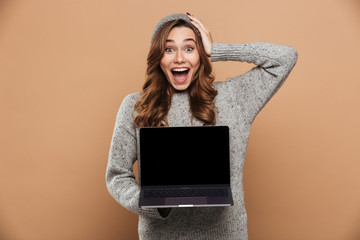 Sticker - Close-up photo of young overjoyed brunette woman in warm clothes holding her head while showing blank laptop screen