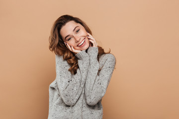 Poster - Portrait of cute smiling brunette girl in soft sweater touching her face while looking at camera