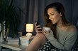 © chika_milan - Caucasian young woman drinking coffee and using smart phone while sitting on bed in bedroom