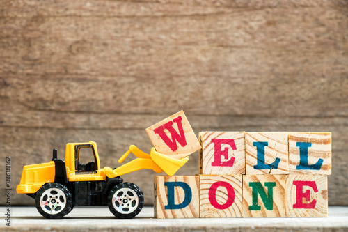 Fotografia Toy bulldozer hold letter block w to complete word well done on wood background