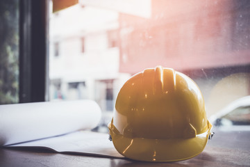 A yellow hard hat on the desk of an engineer.Protective equipment worn to protect the head from dangers of working in a construction site. The concept of Industrial construction and safety.