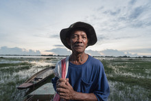 Photo Portrait Of The Elderly Native Fisher,who Are Out Fishing In The River With Boats Background.