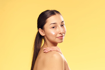 Wall Mural - Beautiful young woman on Yellow background applies cosmetic face cream