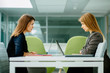 © Iryna - Side view of two business women looking at each other sitting at a table in open space comfortable office. Business, work and people concept.