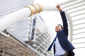 Businessman smiling and raising his fist with number 1 in the air, with office building background - business success, achievement, and win concepts